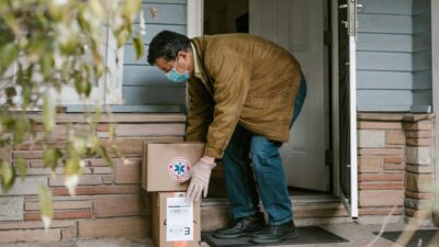 Man wearing mask delivering packages to doorstep for contactless COVID-19 safety.