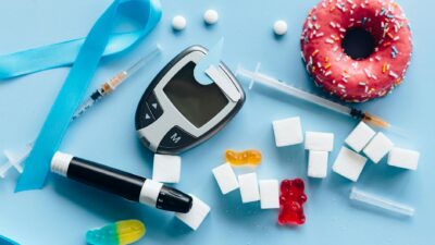 Flat lay of diabetes essentials and sugary food on blue background symbolizing health awareness.