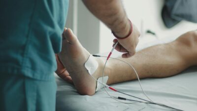 Close-up of a healthcare worker examining a patient's foot with medical equipment in a hospital setting.