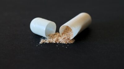 Close-up of a split capsule with powder spilling on a dark surface, symbolizing medicine and health.