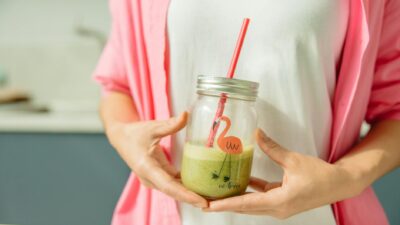 Close-up of a woman holding a green smoothie in a glass jar, promoting healthy living.