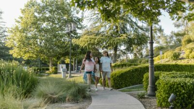 A joyful family walking together on a sunny day in the park, surrounded by greenery.