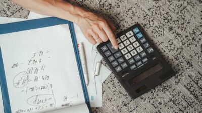 Top view of a hand calculating numbers with a large calculator and notes on a desk.