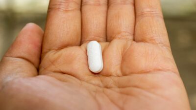 Close-up photo of a hand displaying a single white pill on the palm, symbolizing medication.