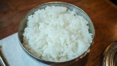 Close-up of steamed white rice in a stainless steel bowl on a wooden table.