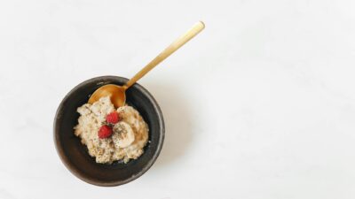 Aerial view of a breakfast bowl with oatmeal, bananas, raspberries, and chia seeds on a white surface.