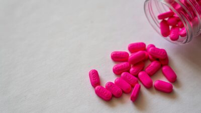 Pink pills spilling from a glass bottle onto a surface, highlighting pharmaceutical care and medication.