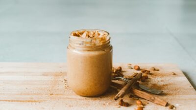 Creamy homemade peanut butter in a jar with cinnamon sticks on a wooden board.