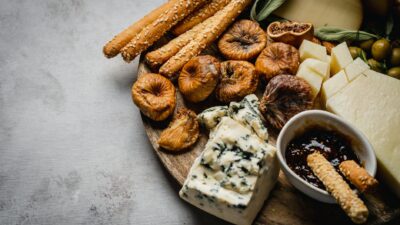 A gourmet cheese platter featuring blue cheese, dried figs, and breadsticks on a wooden board.