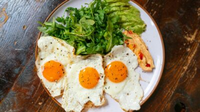 Top view of a breakfast plate with eggs, arugula, avocado, and spread.