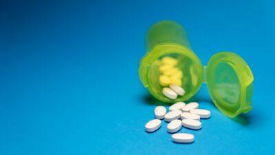 Image of a green pill bottle with white tablets scattered on a blue background, symbolizing healthcare and medication.