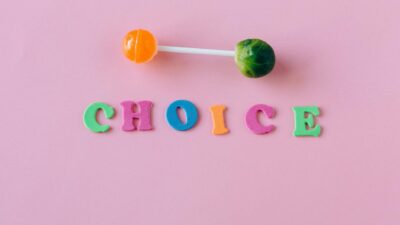 Colorful choice between candy and vegetable on pink background.