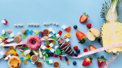 Flat lay of sweets and fruits on blue background with health message 'Eat Less Sugar'.