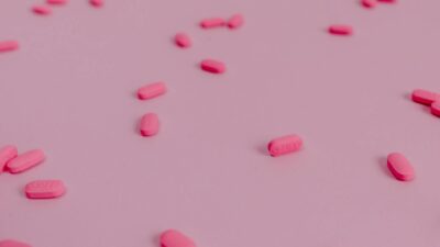A flat lay of vibrant pink pills scattered on a pastel pink surface, perfect for healthcare themes.
