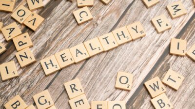 Wooden letter tiles arranged on a wooden surface spelling out 'healthy', symbolizing wellness.