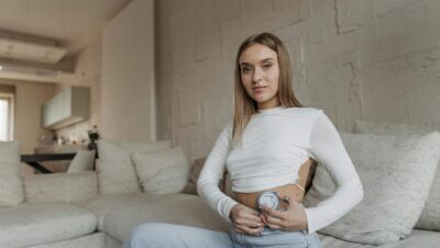 Young woman sitting on a couch managing diabetes with an insulin pump in a cozy home setting.