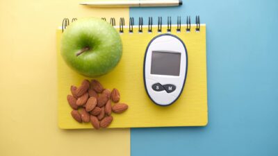 Flat lay of diabetes tools, green apple, almonds, and notebook for health planning.