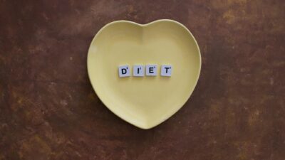 A heart-shaped yellow plate with scrabble tiles spelling 'Diet' on a brown textured background.