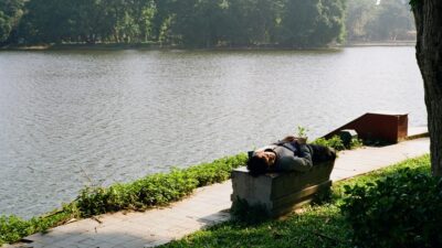 Person sleeping on a bench by the lake.