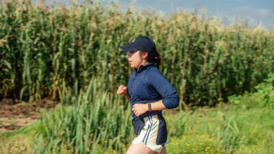 Female jogger running through a rural cornfield on a sunny day.