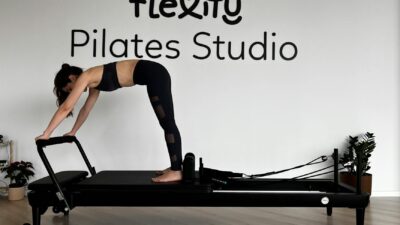 Woman performing Pilates on reformer machine in minimalist studio.