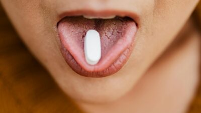 Close-up image of a person placing a pill on their tongue, symbolizing medication or health care.