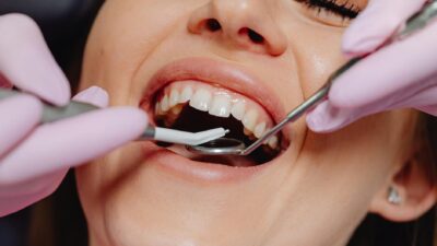 Smiling woman at dentist with tools for dental exam, highlighting dental care.
