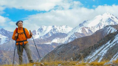 Senior woman hiking in mountainous terrain with snow-capped peaks, enjoying outdoor adventure.