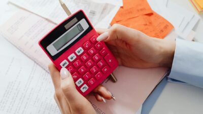 Close-up of hands holding a red calculator, managing finances with documents and receipts.