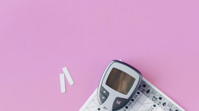 Flat lay of a blood glucose monitor and test strips on a pink surface.