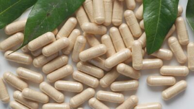Organic medicine capsules with fresh green leaves on a white background.
