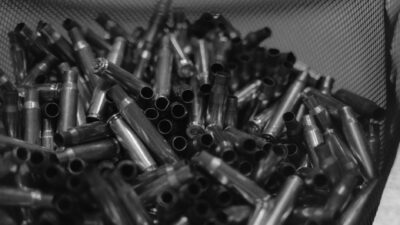 Black and white image of spent bullet casings in a container, emphasizing shooting and military themes.