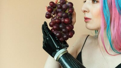 A woman with vibrant colored hair and a prosthetic hand holding a bunch of grapes.