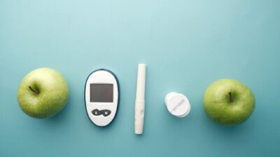 A diabetes testing kit alongside green apples on a blue background, symbolizing health and diet management.