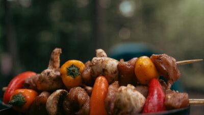 Close-up of grilled meat and colorful vegetables on skewers outdoors, perfect for barbecue lovers.