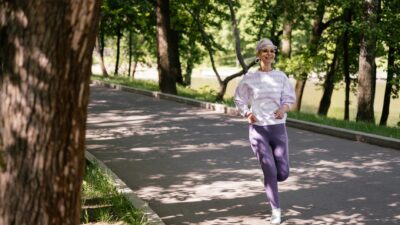 Elderly woman enjoying a refreshing jog in a lush green park during the day.