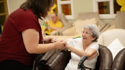 Caregiver assists elderly woman with walker.