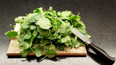 A pile of fresh spinach leaves on a wooden cutting board with a knife nearby.
