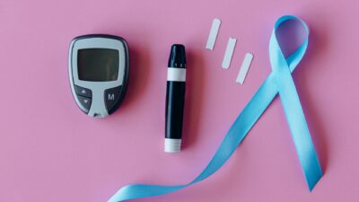 A glucometer with blue ribbon for diabetes awareness on a pink background.