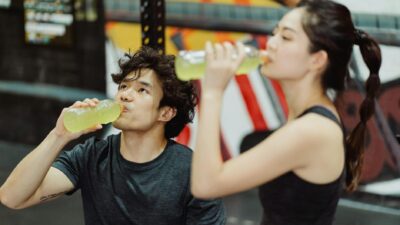 Fit Asian couple hydrating at the gym after an intense workout. Refreshing drink break.