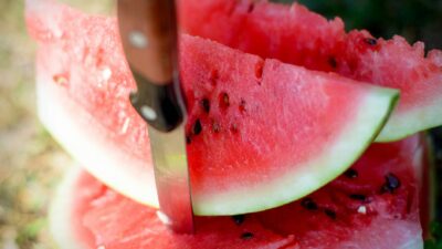 Close-up of a juicy watermelon sliced with a knife outdoors, epitomizing summer refreshment.