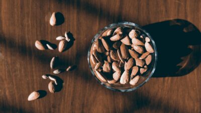 Close-up of almonds in a glass bowl on a wooden surface with dramatic shadows.