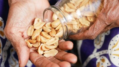 Close-up of elderly hands pouring roasted peanuts from a glass jar into a palm.