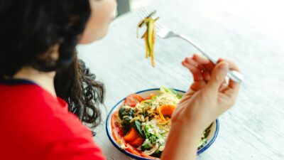 A woman in a red shirt enjoys a fresh salad indoors at a restaurant table.