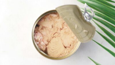 Open can of tuna on a light background with a decorative leaf. Ideal for food packaging visuals.