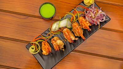 Gourmet grilled shrimp served with fresh vegetables and sauce on a black plate.