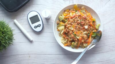 Top view of a nutritious vegetable salad next to diabetic monitoring equipment on a wooden table.