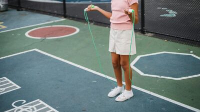 A young girl in summer attire jumping rope on a colorful outdoor court.
