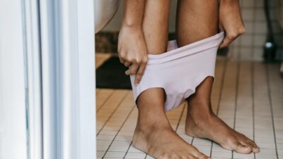 Crop anonymous barefoot ethnic female putting on bikini on tiled floor near toilet at home