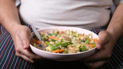 Close-up of an overweight individual holding a nutritious vegetable salad in a pink bowl.